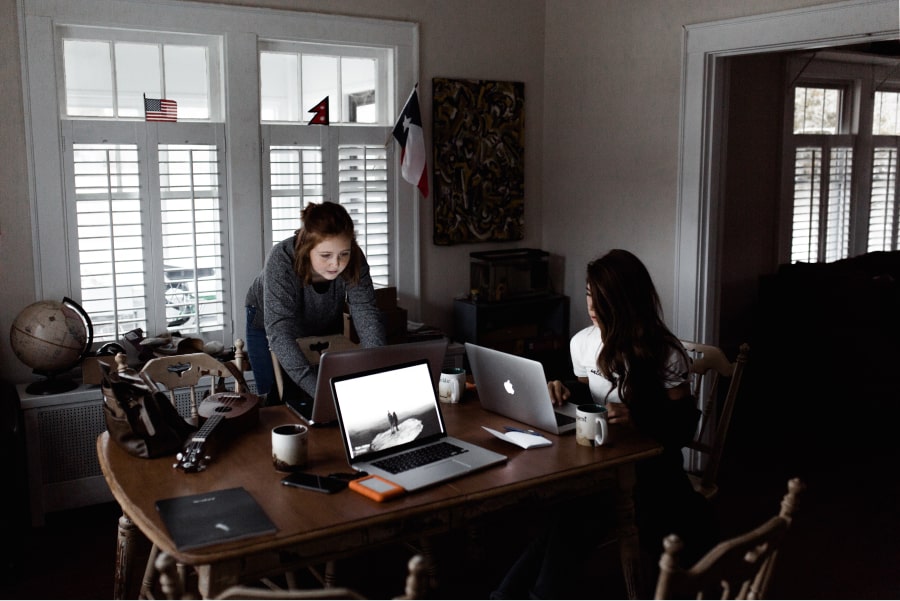 Duas mulheres trabalham nos seus computadores portáteis a partir de casa - Marketing Digital Home Office.